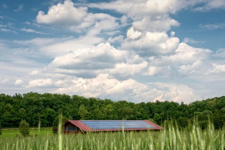 Solar panels on a building in a field under a partly cloudy sky.